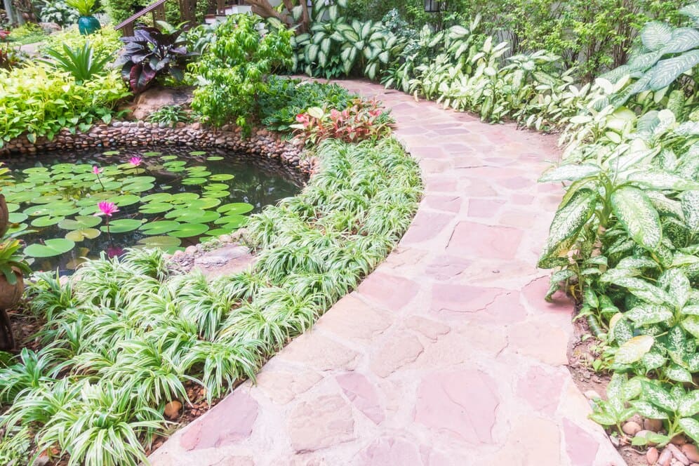 Lát Đá Tự Nhiên – Giải Pháp Bền Đẹp Cho Cảnh Quan Biệt Thự Không Bao Giờ Lỗi Mốt 2 Một lối đi uốn lượn quanh hồ sen trong khu vườn nhiệt đới, được lát bằng đá tự nhiên màu hồng nhạt.