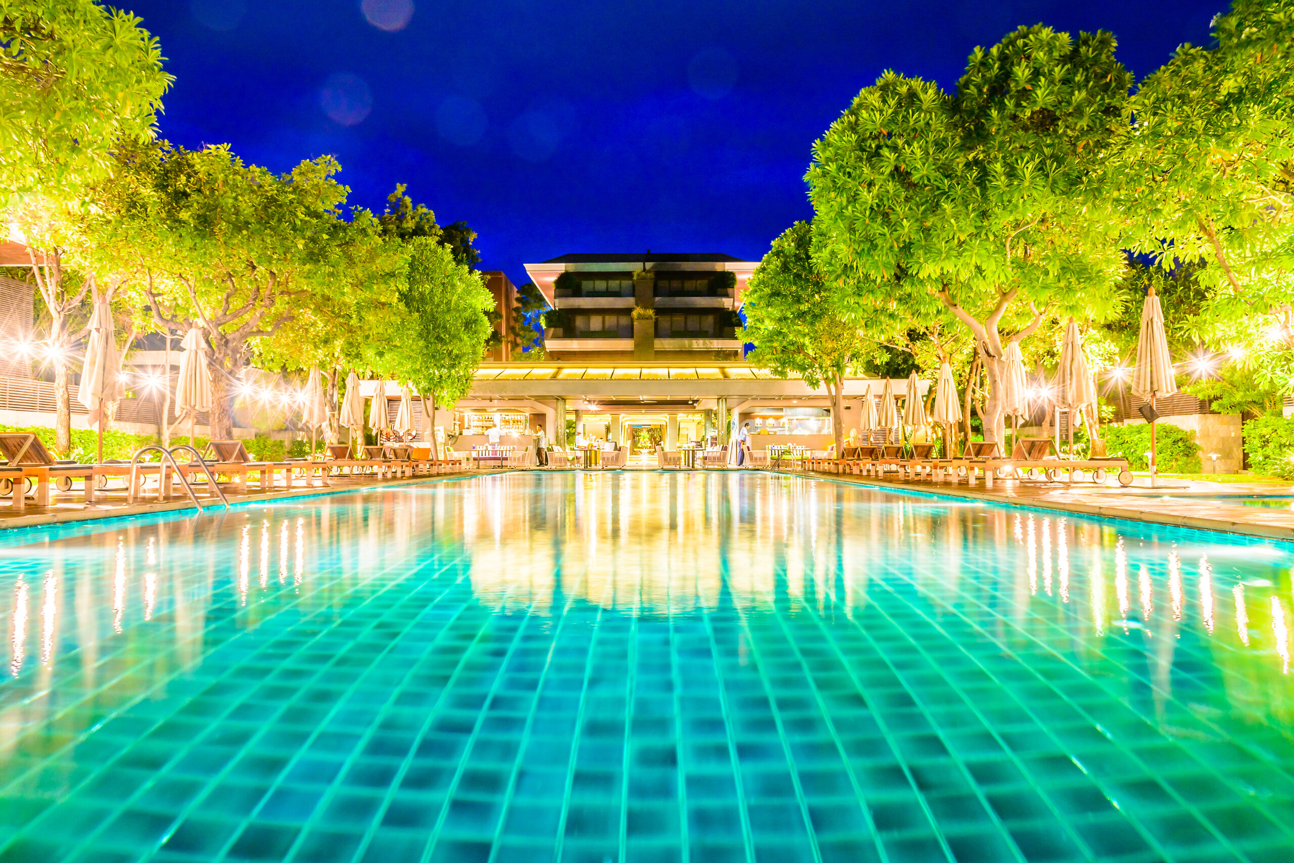Xu Hướng Villa Xanh 2025: Sống Sang Mà Không Tách Rời Thiên Nhiên 4 Biệt thự nghỉ dưỡng hiện đại về đêm với hồ bơi trung tâm, hàng cây xanh mướt và ánh đèn vàng ấm áp.