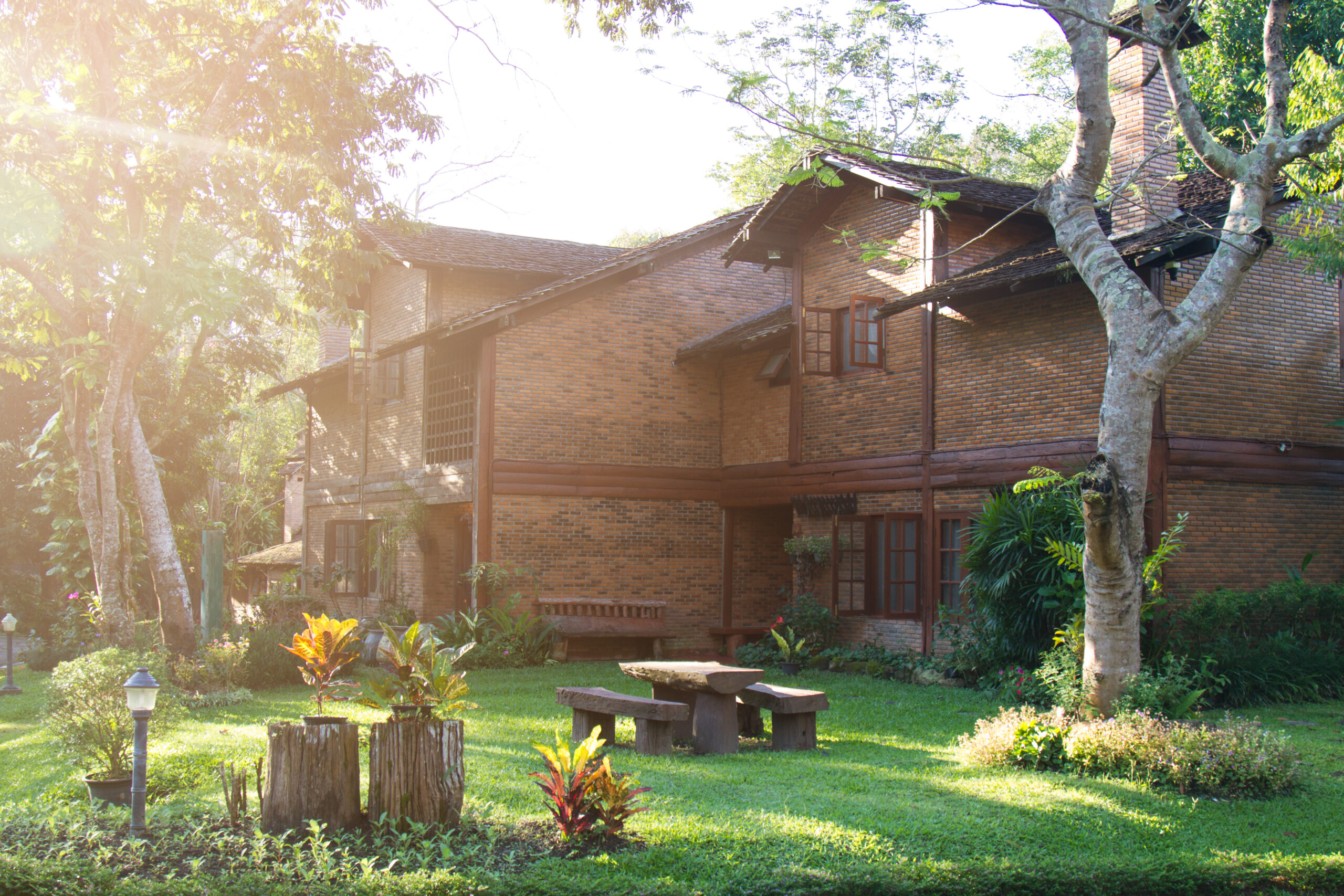 Xu Hướng Villa Xanh 2025: Sống Sang Mà Không Tách Rời Thiên Nhiên 3 Biệt thự gạch mộc giữa khu vườn xanh mát với bàn ghế đá thô, cây xanh và ánh nắng nhẹ xuyên qua tán lá.